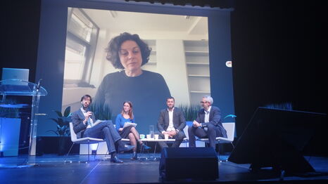 Conférence avec intervenants sur scène et une intervenante en visioconférence