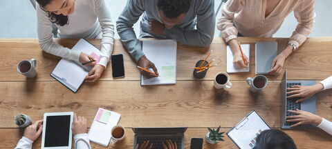 Personnes travaillant ensemble autour d’une table avec ordinateurs et carnets.