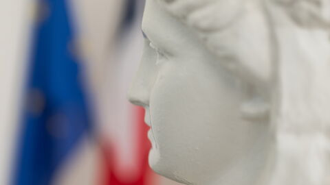 Gros plan sur une sculpture de Marianne avec drapeau français en arrière plan